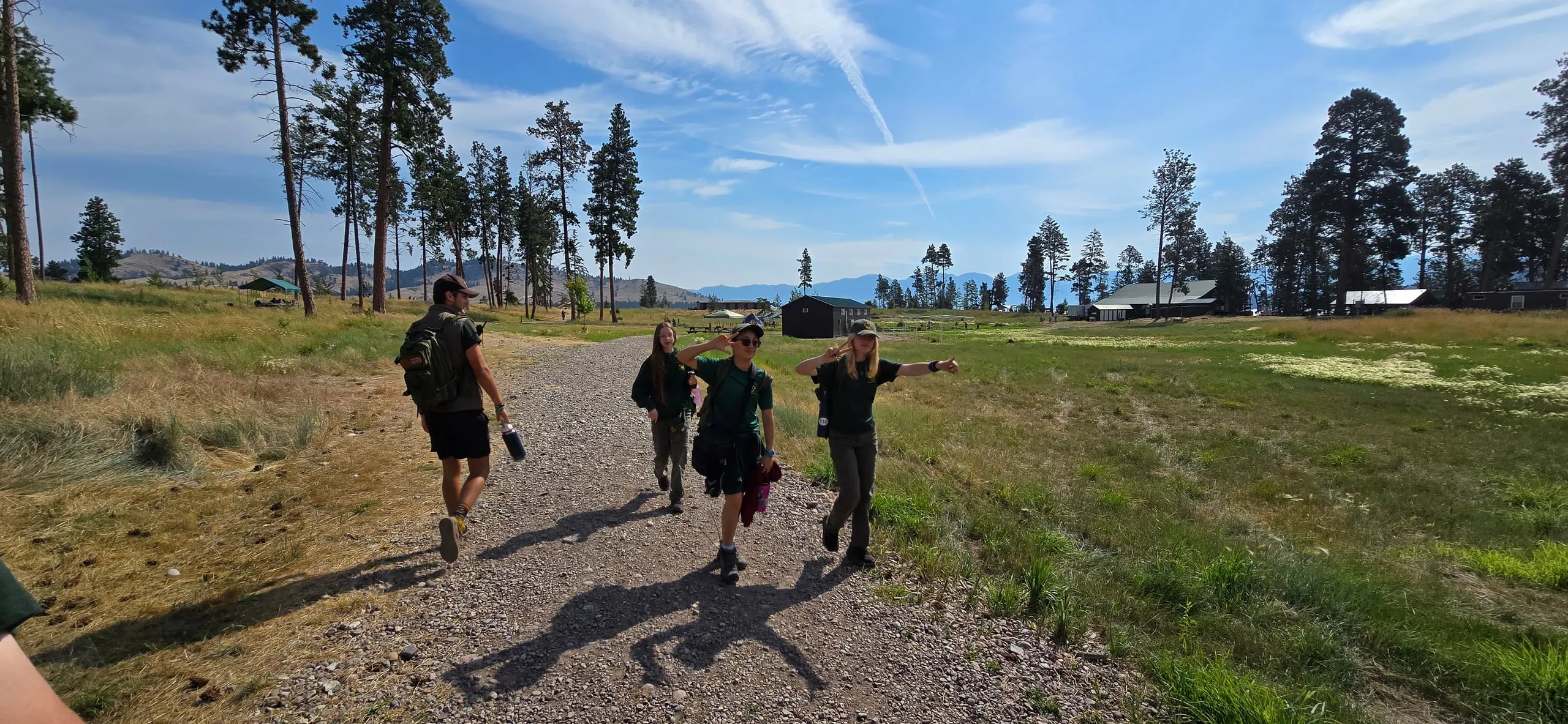 Scouts carrying daypacks walk along a path at camp.