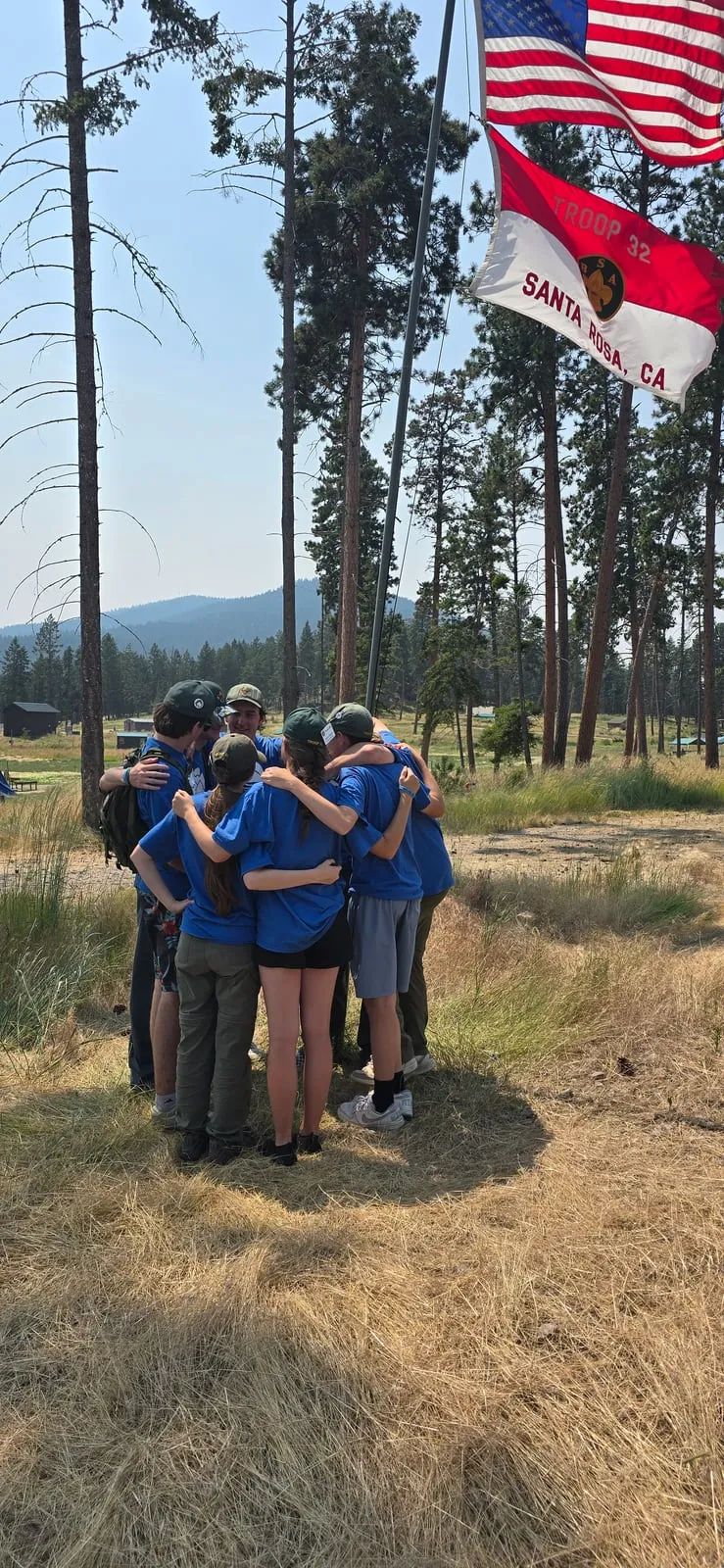 A patrol of Scouts in a huddle, arms around each other, beneath the American flag and the Troop 32 flag.